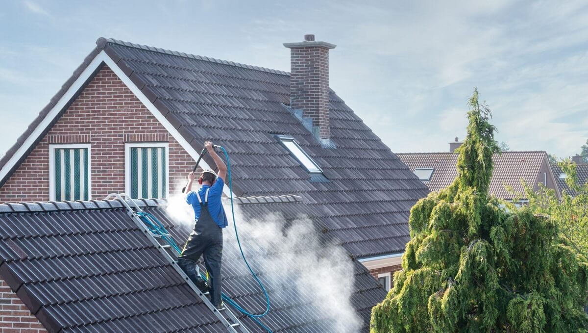 man pressure washing home roof